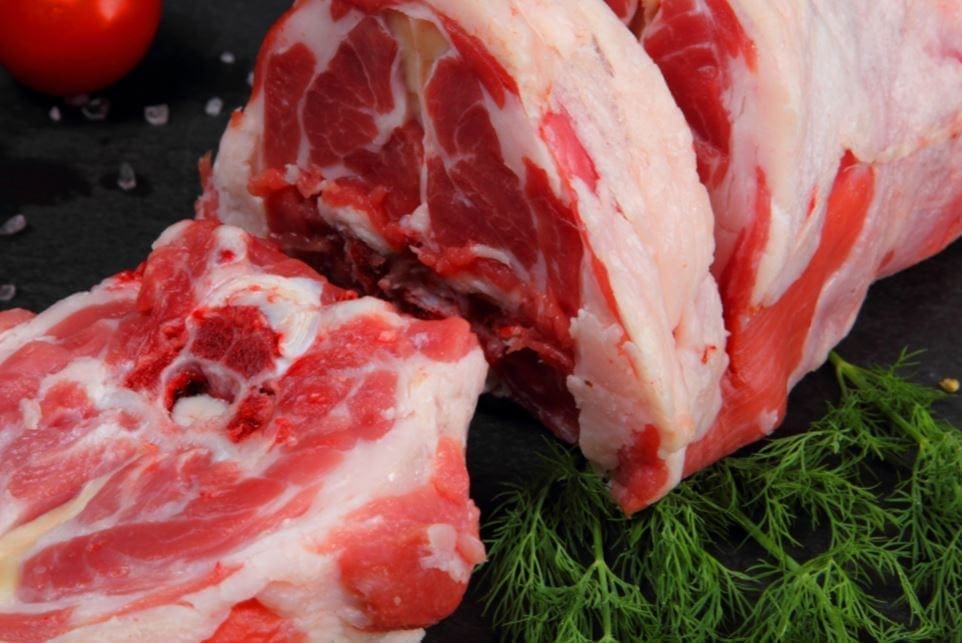Raw marbled meat on dark surface, cut open; fresh dill, coarse salt, tomato in background.
