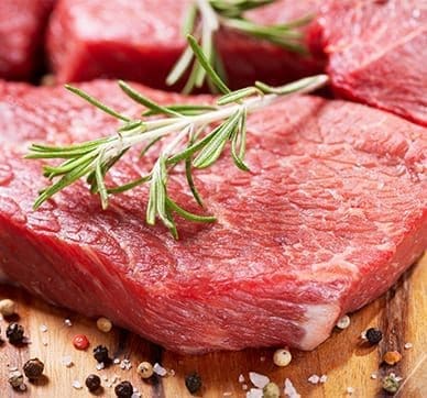 Raw red meat with rosemary and peppercorns on a wooden surface.
