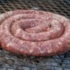 Coiled raw sausage on grill with visible charcoal, ready to be cooked.