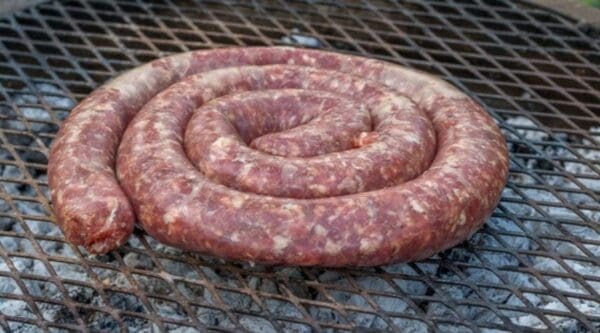 Coiled raw sausage on grill with visible charcoal, ready to be cooked.
