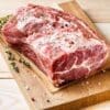 Raw seasoned pork roast on cutting board with thyme, salt, and pepper. Marbled texture.
