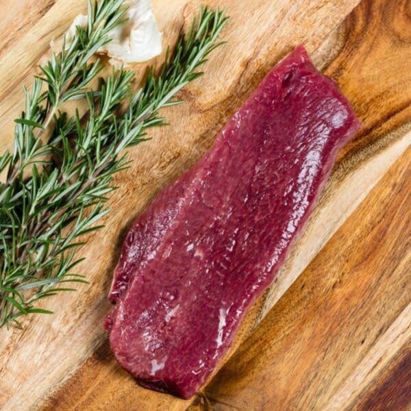 Raw steak on wooden board with rosemary and garlic clove nearby.