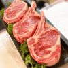 Four ribeye steaks on black tray with green lettuce garnish.