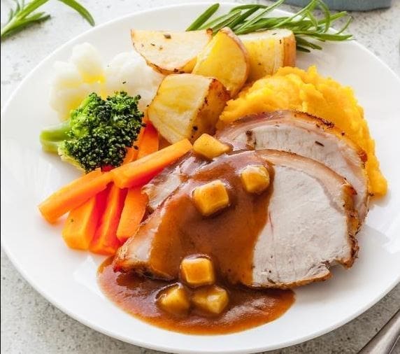 Plate with roast meat, gravy, mashed potatoes, roasted wedges, broccoli, carrots, cauliflower.