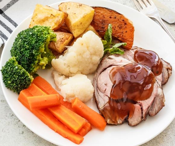 Plate with sliced roast meat, gravy, potatoes, sweet potato, broccoli, cauliflower, carrots.