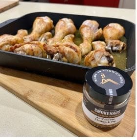 Tray of roasted chicken drumsticks on board with Smokehaus seasoning jar in the foreground.
