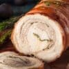 Rolled roasted porchetta with herbs on wooden board, crispy golden-brown exterior.