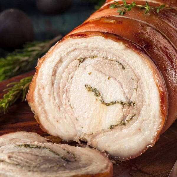Rolled roasted porchetta with herbs on wooden board, crispy golden-brown exterior.