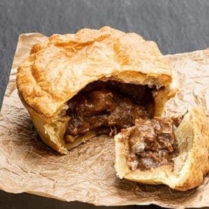 Savory pie with golden crust, revealing meat filling on parchment paper.