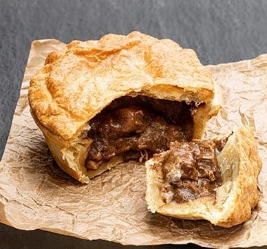 Savory pie with golden crust, revealing meat filling on parchment paper.