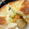 Savory golden-brown pastry with seafood and vegetable filling in creamy sauce, partially cut.