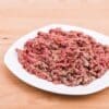 White plate with seasoned raw minced meat on light wooden surface.