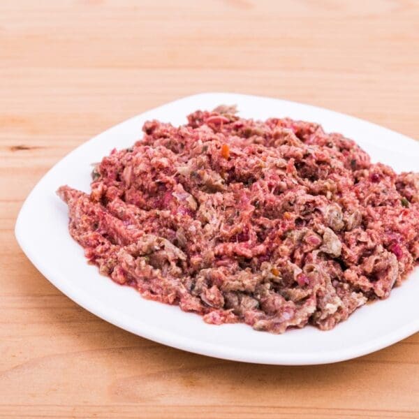 White plate with seasoned raw minced meat on light wooden surface.