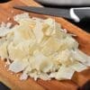 Shaved cheese on wooden board with knife nearby.