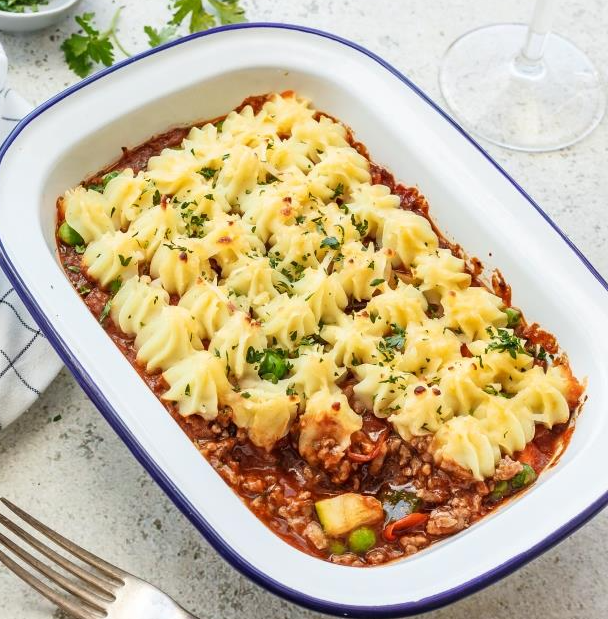 Shepherd's pie with mashed potatoes and herbs in a rectangular dish, fork nearby.