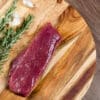 Raw steak on wooden board with rosemary and garlic clove nearby.