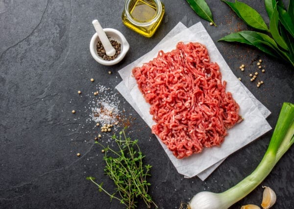 Raw ground meat on parchment paper with herbs, pepper, olive oil, salt, and bay leaves.