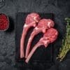 Three raw lamb chops, red peppercorns, and thyme on a black slate surface.
