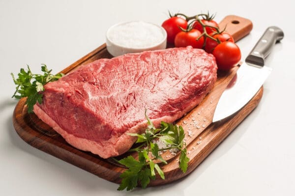 Raw beef steak on a cutting board with knife, parsley, salt, tomatoes.