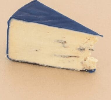 Slice of cheese with smooth interior and blue wax coating on a light surface.