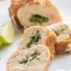 Sliced chicken rolls with herbs and lime wedges on a white plate.
