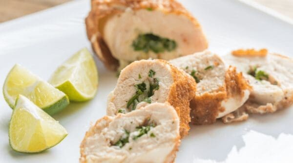 Sliced chicken rolls with herbs and lime wedges on a white plate.