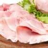Thinly sliced ham on a wooden board with fresh green lettuce leaves.