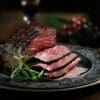 Sliced medium-rare grilled steak on ornate plate, garnished with rosemary sprigs.