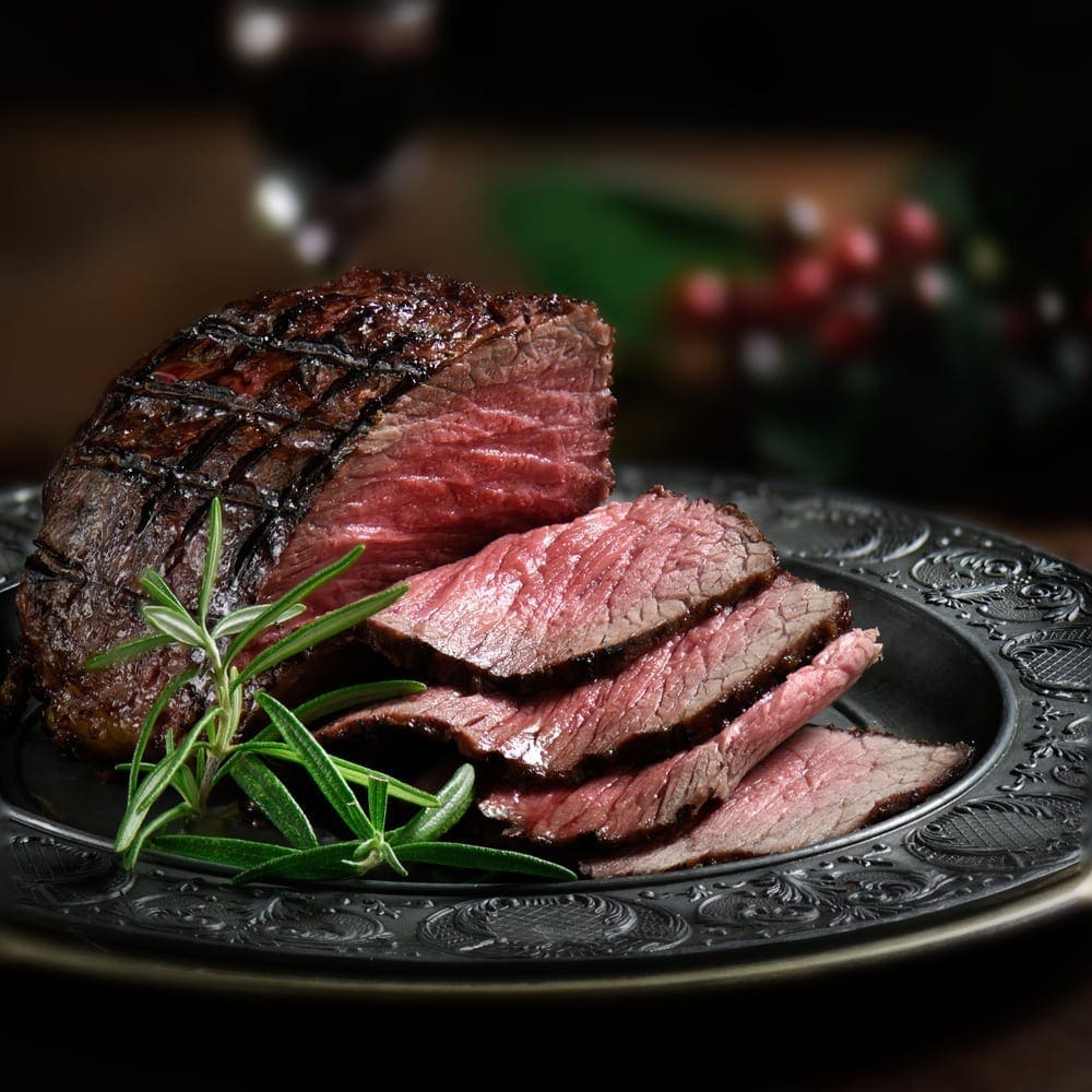 Sliced medium-rare grilled steak on ornate plate, garnished with rosemary sprigs.