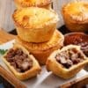 Small round meat pies with golden crusts, one cut open; red sauce bowl in background.