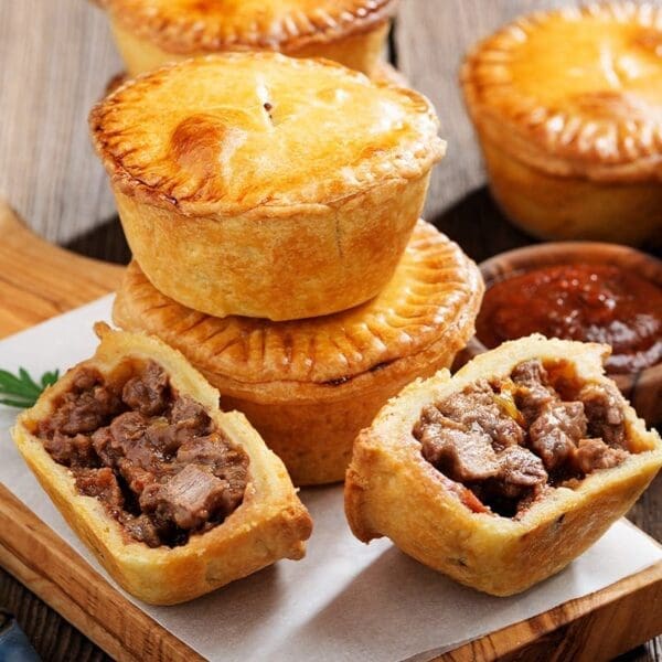 Small round meat pies with golden crusts, one cut open; red sauce bowl in background.