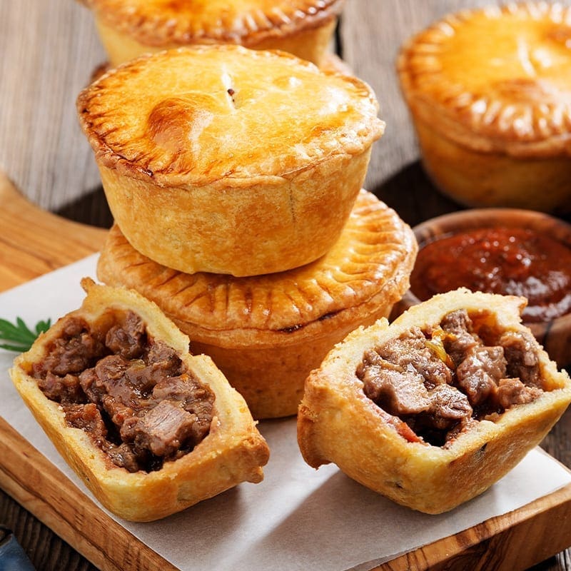 Small round meat pies with golden crusts, one cut open; red sauce bowl in background.