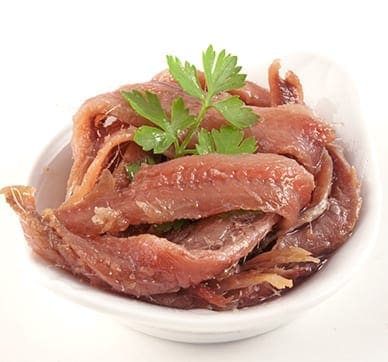 Small white bowl of anchovy fillets garnished with fresh parsley.