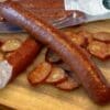 Whole and sliced smoked sausage on cutting board, package in background.