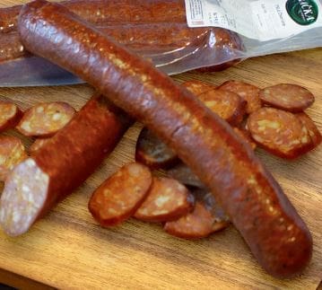 Whole and sliced smoked sausage on cutting board, package in background.