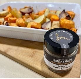 Jar of Smokehaus garlic pepper seasoning in front of roasted vegetables in a white dish.
