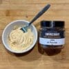 Jar of Smokehaus seasoning and bowl of seasoned butter with spoon on wooden surface.