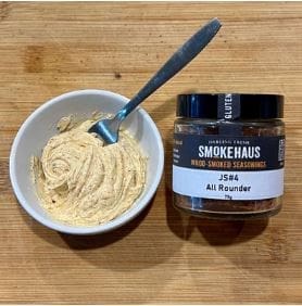 Jar of Smokehaus seasoning and bowl of seasoned butter with spoon on wooden surface.