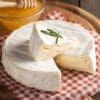 Soft cheese wheel with white rind, sliced to show creamy inside, on checkered cloth with honey.