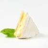Wedge of soft cheese with white rind on a surface, with a green basil leaf beside it.