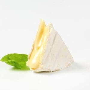 Wedge of soft cheese with white rind on a surface, with a green basil leaf beside it.