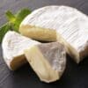Soft cheese with white rind, creamy interior, partially cut on slate with mint sprig.