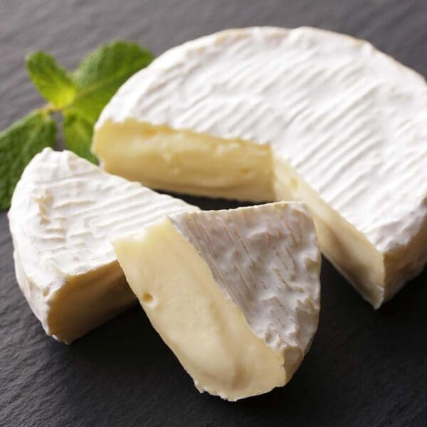 Soft cheese with white rind, creamy interior, partially cut on slate with mint sprig.