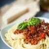 Spaghetti with meat sauce and basil garnish in a white bowl.