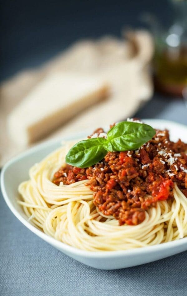 Spaghetti with meat sauce and basil garnish in a white bowl.