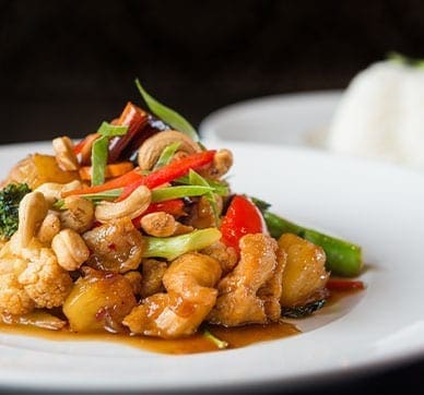 Colorful stir-fried vegetables with cashews on a plate, white rice in the background.