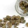 Glass jar tipped over with salted capers on a white surface.