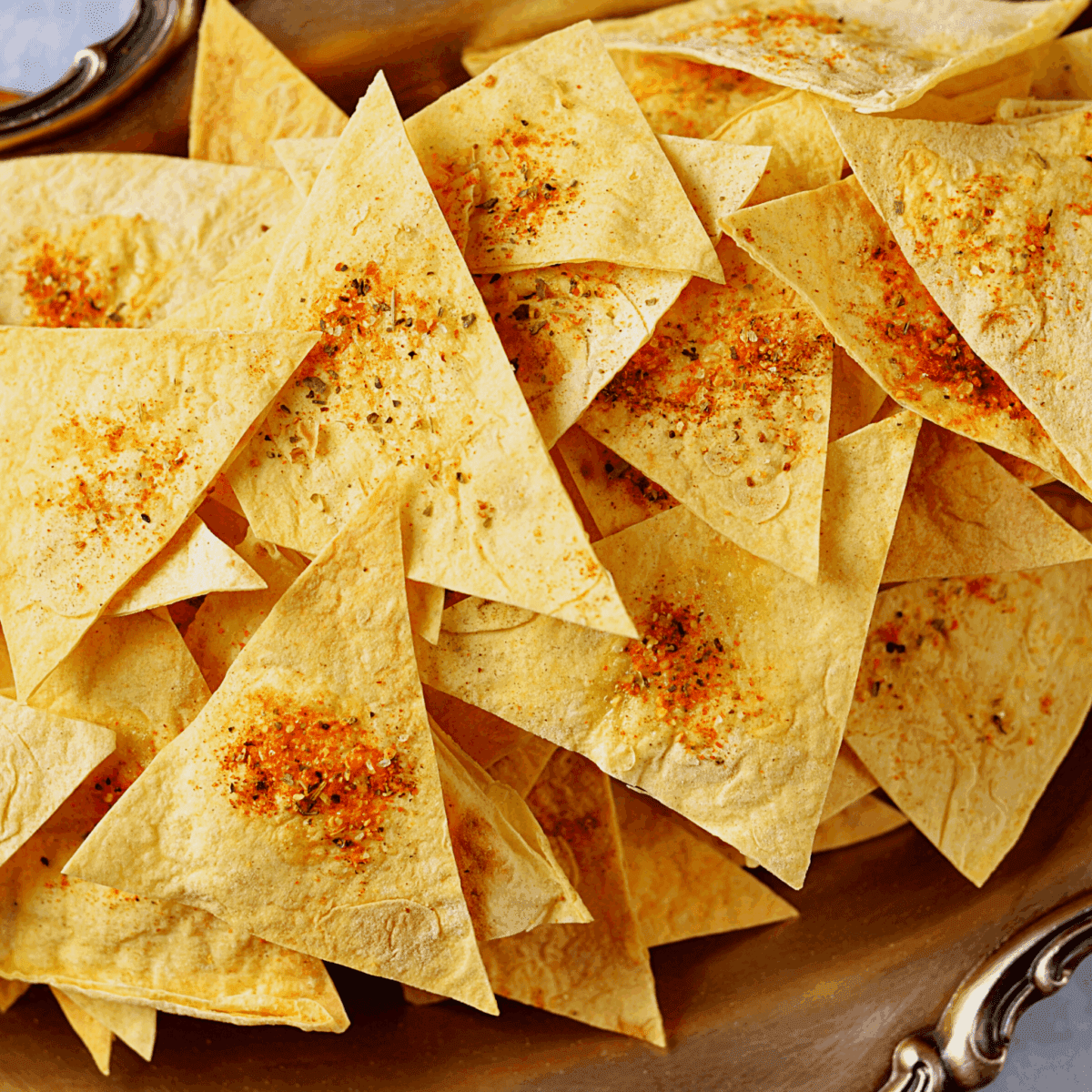 Triangular tortilla chips with spices on a decorative platter.