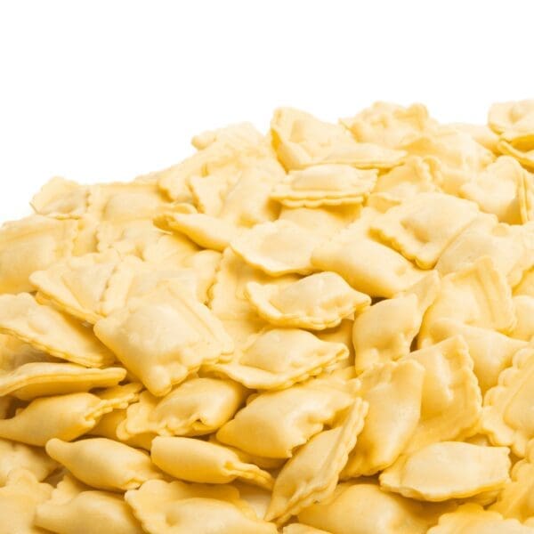 Pile of square, uncooked ravioli with fluted edges on white background.