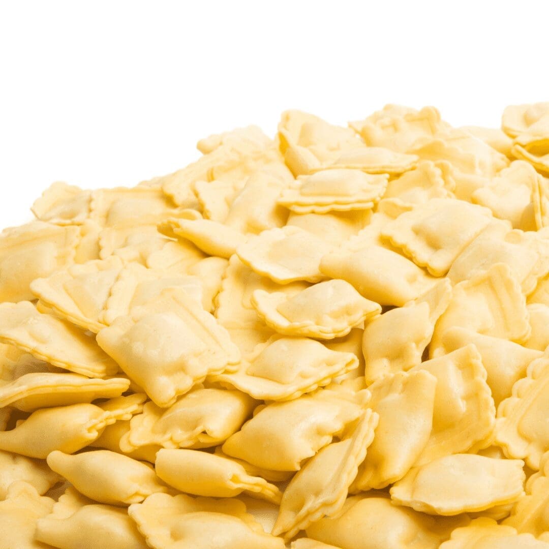 Pile of square, uncooked ravioli with fluted edges on white background.
